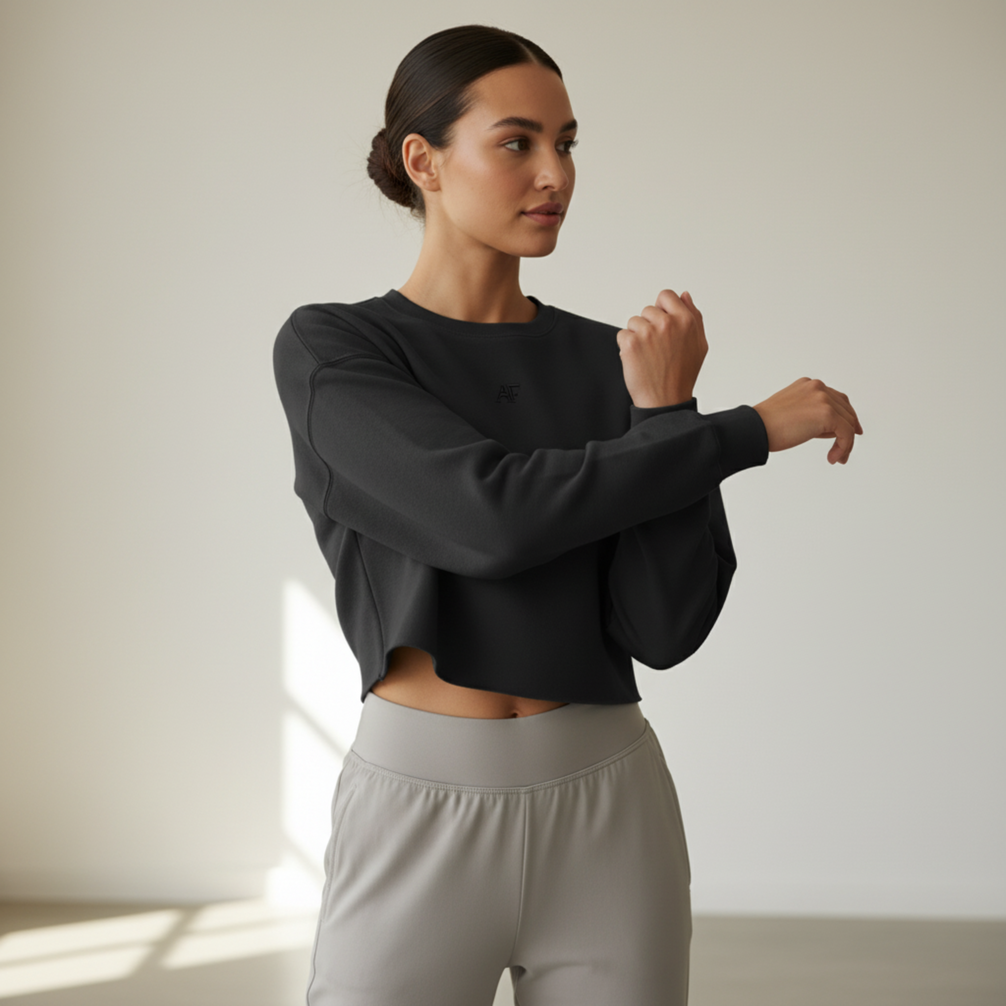 Atlas Form The Hebe Crop in black, minimalist women’s cropped crewneck sweatshirt with tonal black AF logo on the chest, worn in a modern gym studio setting with focus on the sweatshirt.